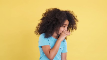 Cheerful Pretty Little Child Keep Secret and Showing Silence Gesture. Share Secrets, Gossip. Whispering in Ear Telling secret. Funny Afro Girl with Curly Hair, isolated on Yellow Background.
