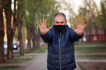 Young guy in a protective black mask on his face looking at camera outdoors, show palm, hand, stop no sign. Air pollution, virus, Chinese pandemic coronavirus concept.