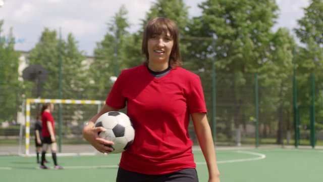 Young female soccer player juggling a ball and then looking at camera and smiling while exercising on outdoor field