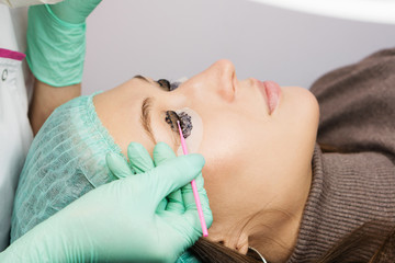 Beauty treatment. Cosmetologist puts black paint on the lashes. Laminating eyelashes. Closeup eyes.