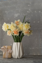 Beautiful bouquet of yellow daffodils in a white vase on a gray table on a neutral background. a gift for mom on mother's day.