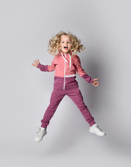 Active kid girl in stylish pink gray sportswear jumps high happy screaming and her curly blonde hair flies