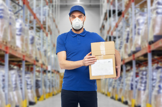 health, safety and pandemic concept - happy delivery man in blue uniform wearing face protective mask or respirator for protection from virus with clipboard over warehouse background