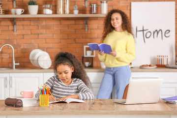 Little African-American girl with her mother doing homework in kitchen