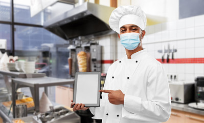 health, safety and pandemic concept - indian male chef cook in toque with tablet pc computer wearing face protective medical mask for protection from virus disease over restaurant kitchen background