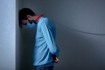 man in medical mask, in a collar on a chain staying depressed in corner