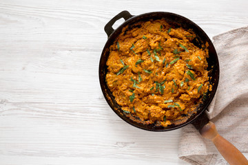 Homemade Chicken Tikka Masala in a cast iron pan on a white wooden background, top view. Flat lay, overhead, from above. Space for text.