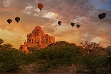 Buddhist Temple at Sunrise with hot air ballon in a golden cloudy sky suronded by bushes in Bagan, Myanmar