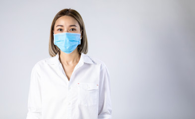 Studio portrait of Asian woman wearing face medical surgical mask, looking at camera, isolated on white background. Mask protection against virus. Covid-19, coronavirus pandemic