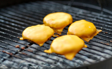 cooking, barbecue and fast food concept - close up of burger meat cutlets with processed cheese roasting on brazier grill outdoors