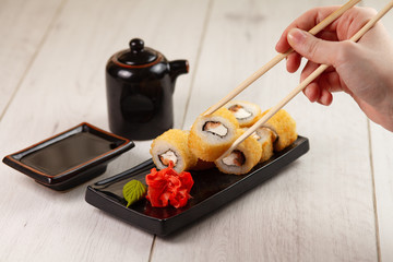 Fototapeta na wymiar Hand holds chinese chopsticks with sushi on food background