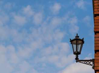 Beautiful transparent lantern with forged details on a background of blue sky with clouds.