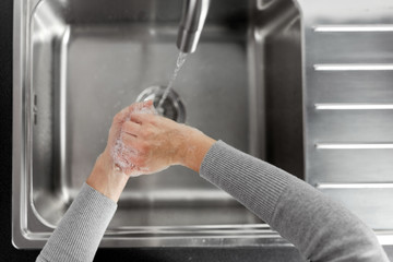 hygiene, health care and safety concept - close up of woman washing hands with soap and water in kitchen at home