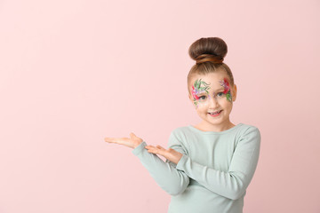 Funny little girl with face painting showing something on color background