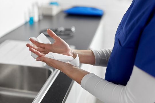 hygiene, health care and safety concept - close up of female doctor or nurse drying hands with paper tissue at hospital