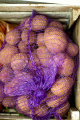 Polypropylene net sack with organic potatoes in a wooden box.