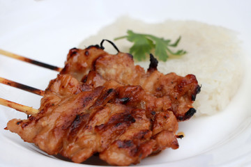 Three Grilled pork skewers with sticky rice on the white plate.