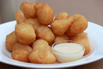Chinese doughnut stick with Sweetened condensed milk in the small glass cup on the white round dish.
