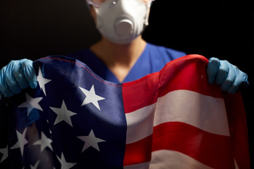 Fototapeta premium medicine, health and pandemic concept - young female doctor or nurse wearing goggles and face protective mask or respirator for protection from virus holding flag of america over black background