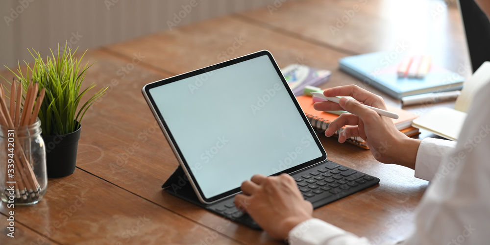 Poster cropped image of graphic designer's hands holding a stylus pen and typing on computer tablet with ke