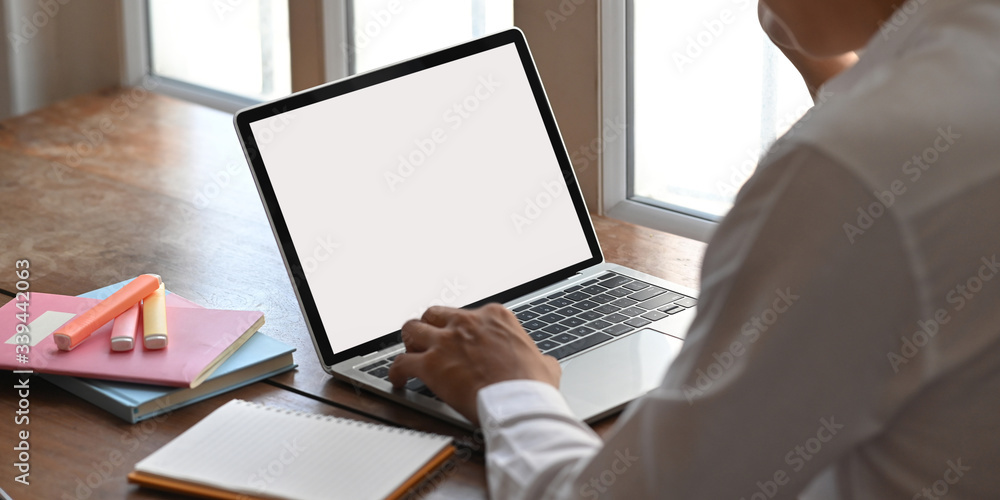 Poster closeup image of smart man typing on computer laptop with white blank screen while sitting at the wo