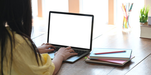 Closeup stylish woman typing on computer laptop with white blank screen while sitting at the wooden working desk over comfortable living room as background.