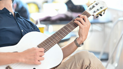 Fototapeta premium Cropped image of smart man relaxing by playing an acoustic guitar while sitting at the modern chair over comfortable sitting room as background.