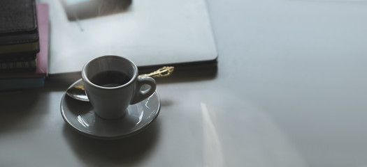 Close-up image of hot coffee cup putting together with spoon on small dish over stack of books as background. Orderly workspace concept.