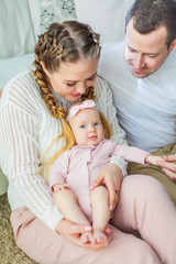 Beautiful young parents are holding their little newborn daughter in their arms. Blue-eyed little girl of 2 months. Baby