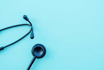 Black modern stethoscope on light blue background, close up.