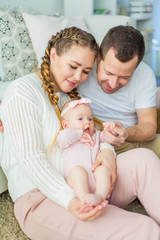 Beautiful young parents are holding their little newborn daughter in their arms. Blue-eyed little girl of 2 months. Baby