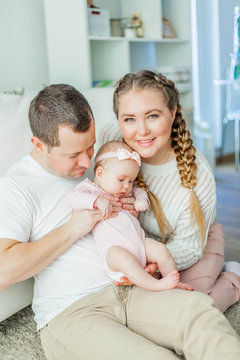 Beautiful young parents are holding their little newborn daughter in their arms. Blue-eyed little girl of 2 months. Baby