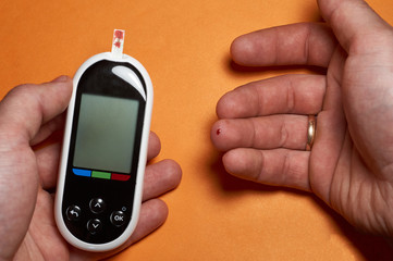 A diabetic checks his blood sugar. Close up man hands self-tested with a Lancet and a glucometer at home.