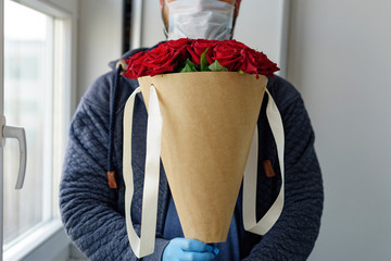 contactless flower delivery, male courier in a protective face mask, medical gloves with a bouquet of red roses, the concept of the decline of the flower business