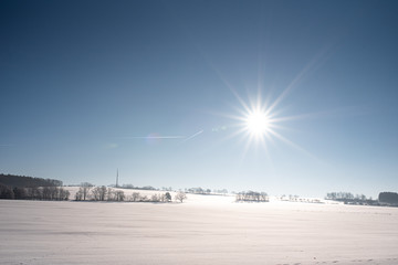 Feld im Winter mit Schneedecke, Sonnenschein und blauem Himmel