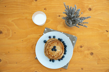 Homemade pancakes arranged on a white plate with blueberries on the table - Copy space