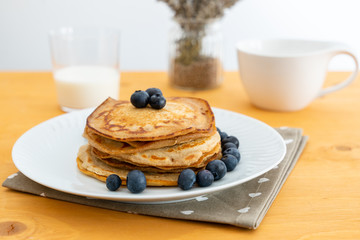 Homemade pancakes arranged on a white plate with blueberries on the table - Copy space