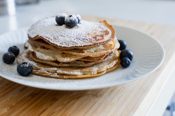 Homemade pancakes with icing sugar arranged on a white plate with blueberries in the kitchen - Copy space