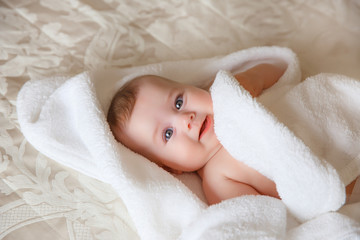 baby is wearing diapers and a white towel in bedroom. A newborn baby is resting in bed after a bath or shower. Children's room. Textiles and bedding for children.