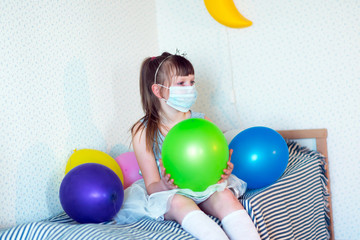 Fototapeta na wymiar girl in medical mask with colorful balloons celebrating her birthday alone at home , isolation concept