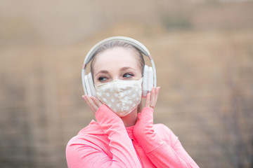 Young girl in a face mask and headphones walking in the park. The new recommendation - everyone to wear masks in public during the coronavirus covid-19 pandemic.