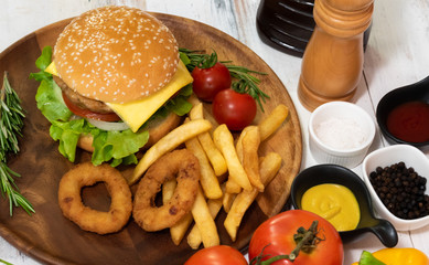 Homemade fresh tasty hamburger side dish with tomato, french fries, ketchub, mastard, salt and pepper on wood plate with white wooden plank background