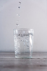 Drops of water from above into a glass of water on a white background. Drink macro photography