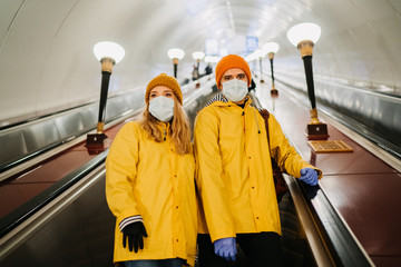 .Couple in medical protective masks dressed in yellow windbreakers going down to subway by escalator. Sad thoughts about pandemic coronavirus. Covid-19 virus concept.