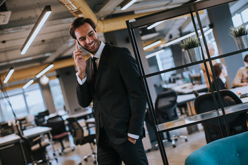 Young businessman wearing black suit using modern smartphone in the office