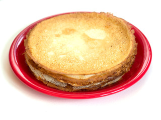 Staple of wheat golden yeast pancakes or crepes on red plate on a white background closeup