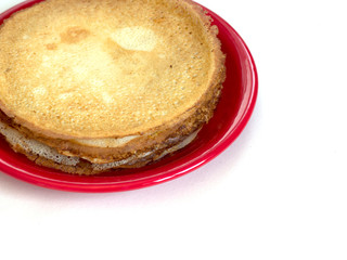 Staple of wheat golden yeast pancakes or crepes on red plate on a white background closeup