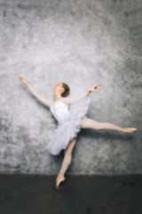 Pretty young ballerina dancer dancing classical ballet against rustic wall