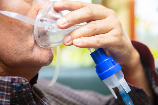 Senior man using medical equipment for inhalation with respiratory mask, nebulizer