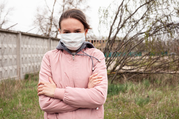 Girl in a medical white mask. Dressed in a pink jacket, in the background a concrete fence, grass and trees. Quarantine time.
Portrait photo, photo for inscription.
